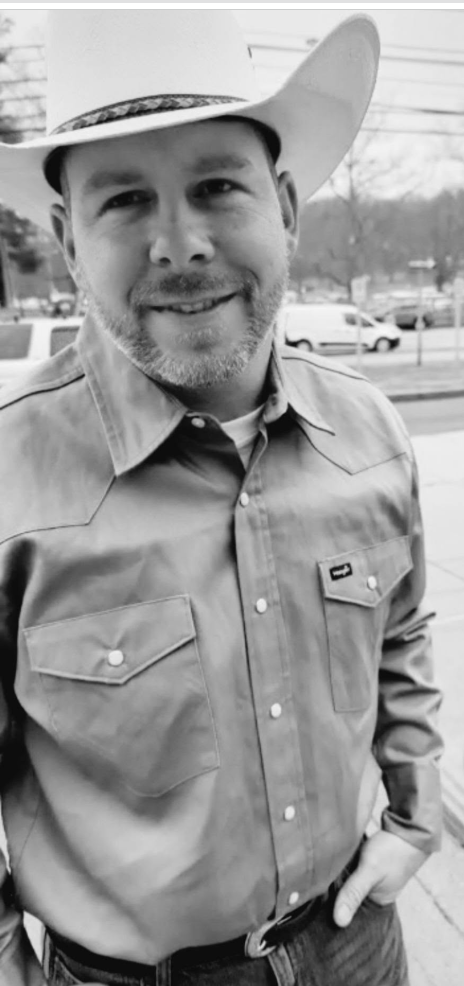 Justin wearing a cowboy hat and button-front shirt outdoors.